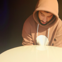 Pixar’s 3d style young man looking down with a white plush cap and brim front faced. Brown sweatshirt with hood and drawstring. Medium-sized beard all over the face. Shy laughter in the corner of his mouth. Gold hoop earring in the ear and black hoop piercing in the nose. Brown eyes and short hair. Skin is white and face is slightly rounded. Diagonal view facing left.